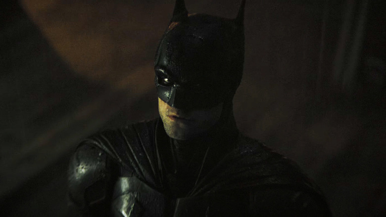 Batmanul lui Robert Pattinon se uită în sus în timp ce stă în ploaie în Batman