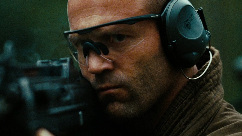 Jason Statham în rolul lui Arthur Bishop purtând căști în timp ce trage o armă în mecanic