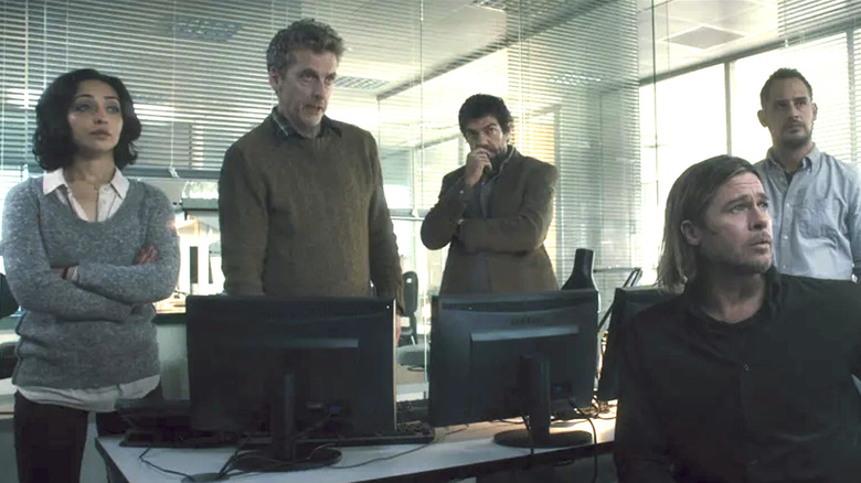 Războiul Mondial Z, echipa OMS care se uită la ecranul TV