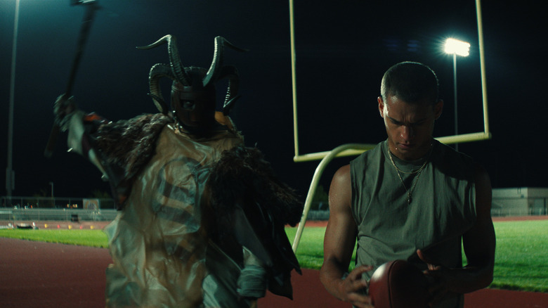 Un bărbat îmbrăcat ca un diavol cu ​​coarne ridică un ciocan pentru a -l ataca pe Cam Cade în el