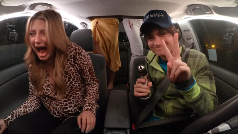 Joe Keery în rolul lui Kurt Krunkle ținând două degete într -un semn de pace și ținea un exercițiu în timp ce Mischa Barton în timp ce Londra țipă pe scaunul de lângă el în Spree