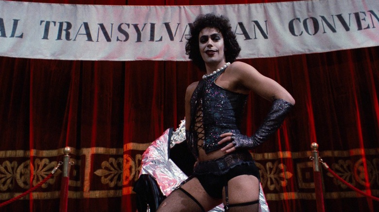 Dr. Frank-N-Furter pozând în fața unui banner în The Rocky Horror Picture Show