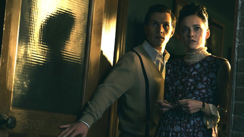 Madison Lawlor ca tânără Lorraine Warren și Orion Smith, ca tânără Ed Warren, stând lângă o ușă deschisă în Conjuring: Ultimele rituri