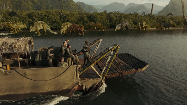 Echipa de pe barcă uitându -se la diverse dinozauri de pe țărm în războiul primitiv