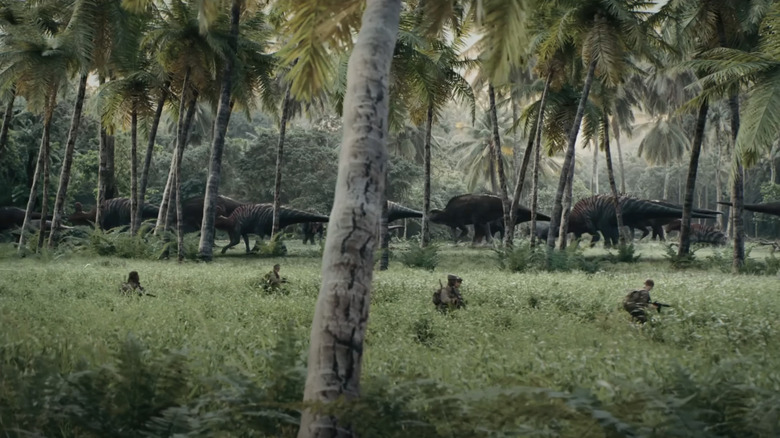 Soldații se plimbă prin iarbă înaltă, în timp ce dinozaurii se opresc în fundal în război primitiv