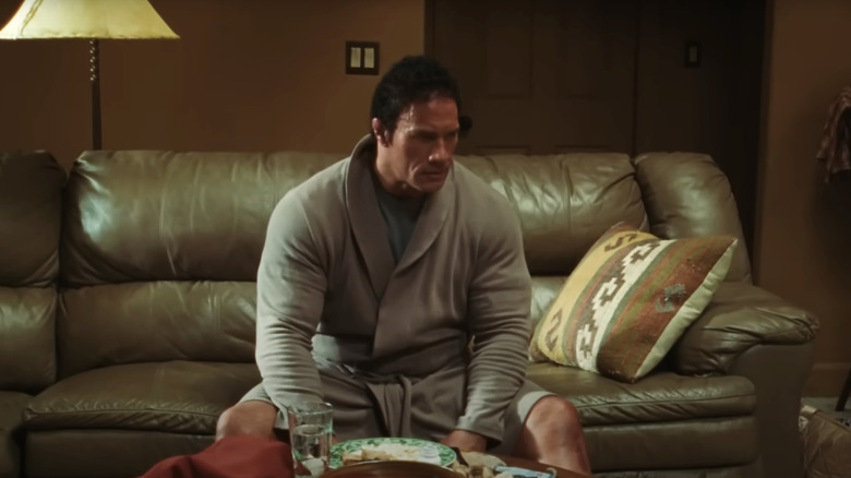 Dwayne Johnson în rolul lui Mark Kerr stând într -o haină pe canapea în mașina de zdrobire