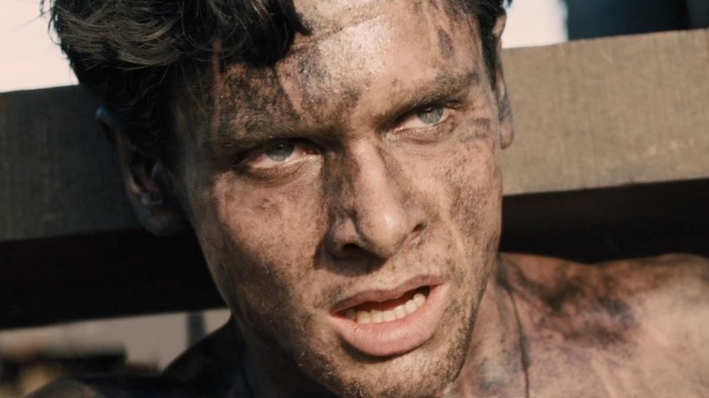 Jack O'Connell ca Louis "Louie" Zamperini în neîntrerupt cu lemn deasupra umerii și acoperit de murdărie