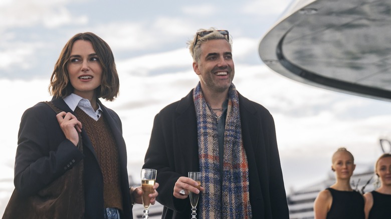 Lo și Adam ținând pahare de șampanie care se uită în jur pe navă în femeia din cabina 10