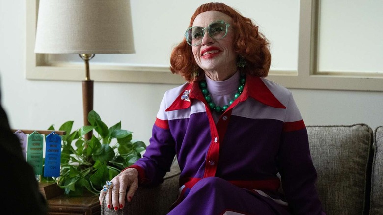 Gladys zâmbind cu ochelari verzi în biroul lui Marcus despre Arme