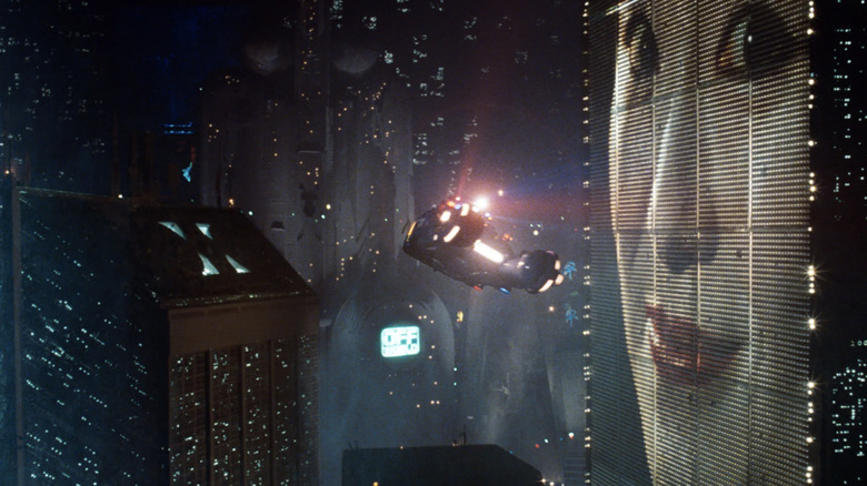 Captură largă a orizontului Los Angeles-ului în Blade Runner, inclusiv o mașină care zboară prin aer și o femeie pe un panou gigant