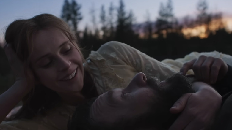 Felicity Jones în rolul Gladys Grainier îl privește pe Joel Edgerton în rolul lui Robert Grainier în timp ce stau întinși împreună afară în Train Dreams