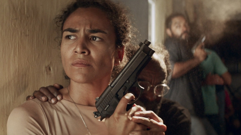 Luciana Souza în rolul lui Isa ridică un pistol în timp ce stă cu spatele la un perete în Bacurau