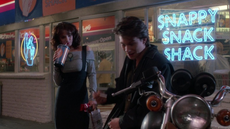 Winona Ryder în rolul lui Veronica bea un Slurpee în timp ce Christian Slater în rolul lui JD se sprijină pe motocicleta sa în Heathers