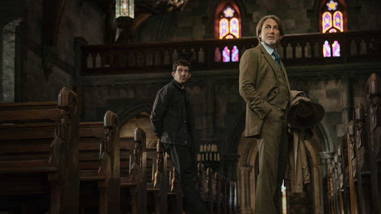 Benoit Blanc și părintele Jud stau într-o biserică, privind în afara camerei în Wake Up Dead Man