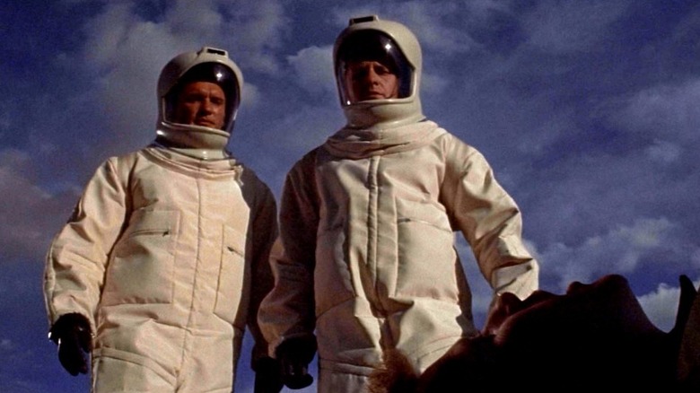 Doi medici îmbrăcați în costume de materii nocive care se uită la un cadavru din The Andromeda Strain