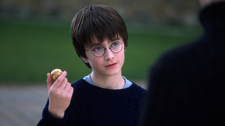 Harry ridică Snitchul de Aur din Harry Potter și Piatra Vrăjitorului