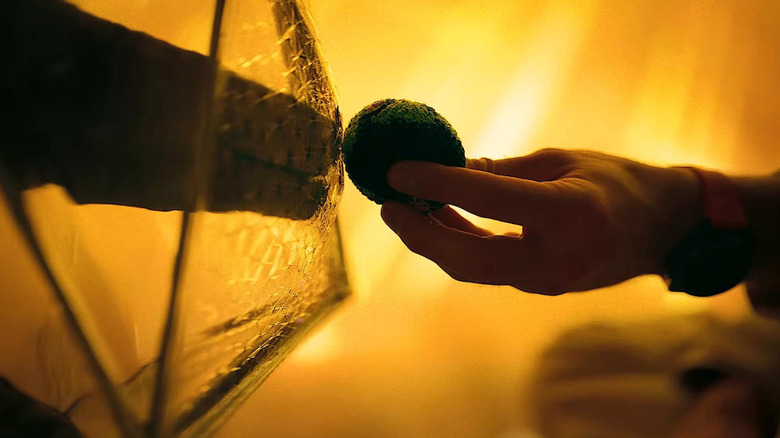 Ryan Gosling în rolul lui Ryland Grace, întinzându-i lui James Ortiz o minge în formă de Pământ ca vocea lui Rocky în Project Hail Mary