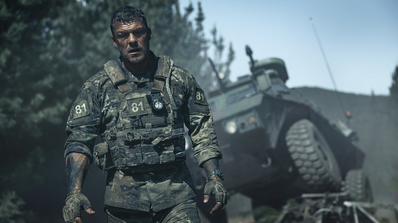 Soldatul 81 stând în haine cu un vehicul militar în spatele lui în War Machine