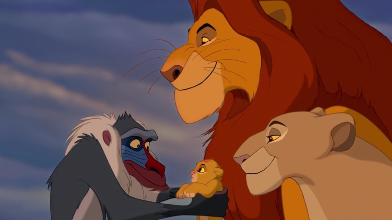 Rafiki îl ține pe Simba în brațe în timp ce mama și tatăl lui se uită în The Lion King