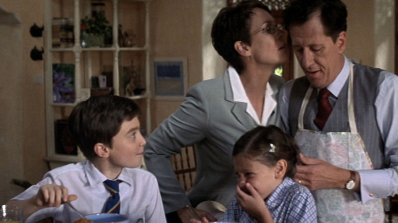 Louisa Pendel de la Jamie Lee Curtis îl sărută pe Harry Pendel de la Geoffrey Rush în timp ce Mark Pendel de la Daniel Radcliffe se uită la ceasuri și Sarah Pendel de la Lola Boorman mănâncă cereale într-o bucătărie în The Tailor of Panama