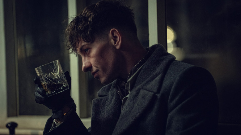 Barry Keoghan în rolul lui Duke purtând o haină și susținând un pahar de whisky în Peaky Blinders: The Immortal Man