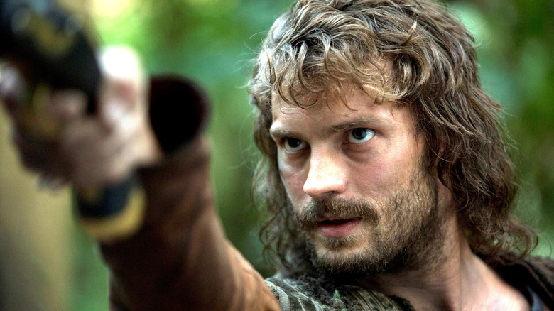 Jamie Dornan în rolul lui Abe Goffe, cu părul lung și barbă și ținându-și brațul sus într-o pădure din Lumile Noi