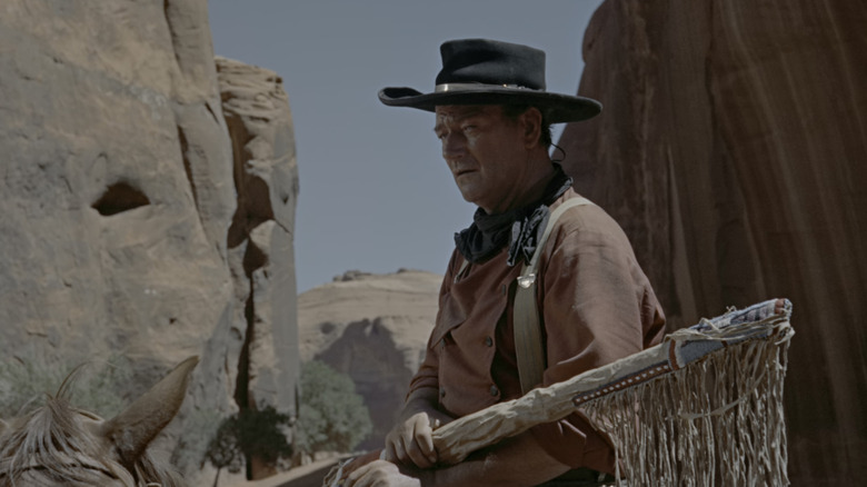Ethan Edwards al lui John Wayne stă pe un cal într-un peisaj stâncos în The Searchers