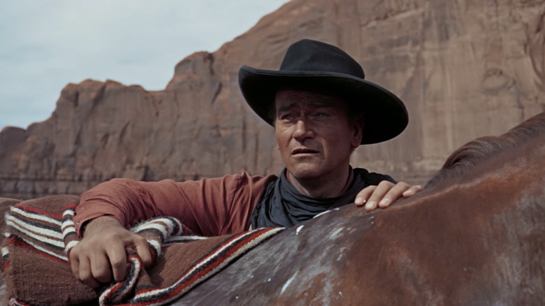 Ethan Edwards al lui John Wayne își sprijină brațele pe cal în timp ce privește în depărtare în The Searchers
