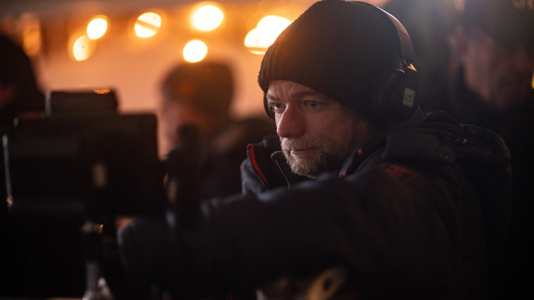 Regizorul André Øvredal stând lângă o cameră în fața luminilor portocalii pe platoul de filmare Passenger