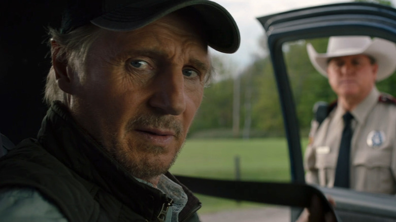 Jim Hanson al lui Liam Neeson stă pe scaunul șoferului mașinii sale, în timp ce un ofițer de poliție stă la fereastra lui în The Marksman