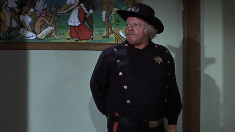 Tobaccy al lui Alan Hale Jr se uită în dreapta lui în timp ce stă pe un hol în There was a Crooked Man
