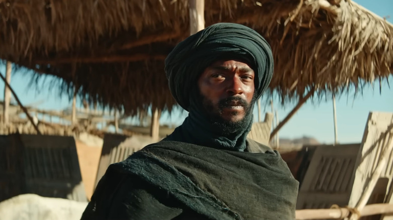 Anthony Mackie ca banditul care stă în fața unei cabane de iarbă din Desert Warrior