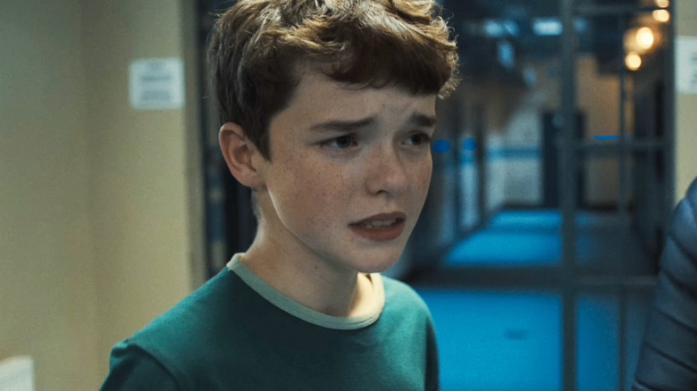 Jamie Miller din Owen Cooper pare îngrijorat în timp ce stă pe holul unei secții de poliție din Adolescență