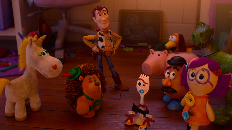 Tom Hanks ca vocea lui Woody stând pe podeaua unui dormitor pentru copii cu alte câteva jucării în Toy Story 5