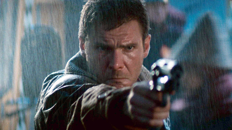 Harrison Ford în rolul lui Deckard ținând pistolul în ploaie în Blade Runner