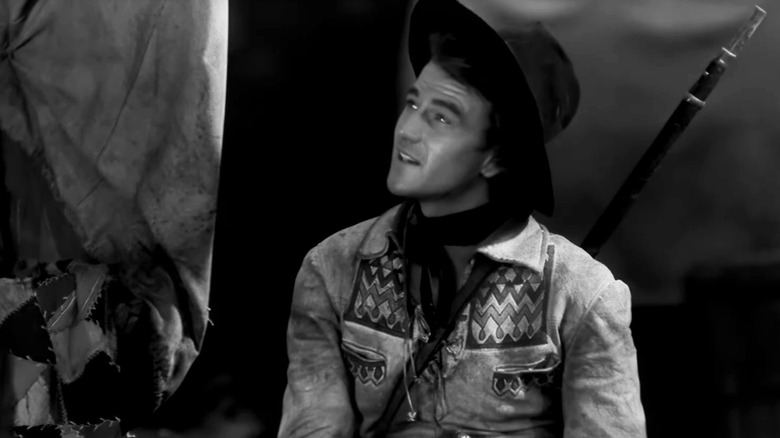 Breck Coleman al lui John Wayne ridică privirea în timp ce stă în The Big Trail
