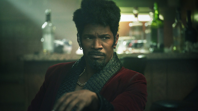 Jamie Foxx în rolul lui Slick Charles stând la o masă cu o băutură în They Cloned Tyrone
