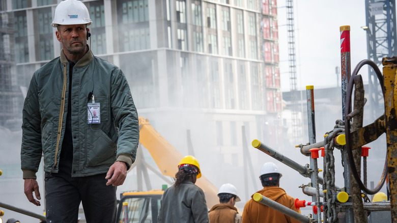 Jason Statham ca Levon Cade purtând o cască de protecție și mergând printr-o zonă de construcție în A Working Man