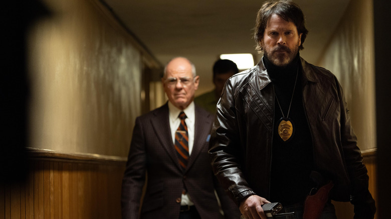 Cary Elwes în rolul detectivului Michael Grable purtând o jachetă de piele și mergând pe un hol ținând un radio, urmat de alți doi în Dead Man's Wire