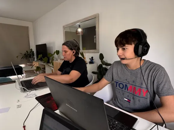 Fotografie a doi participanți la mini-hackathon care participă pe computerele lor din aceeași locație.