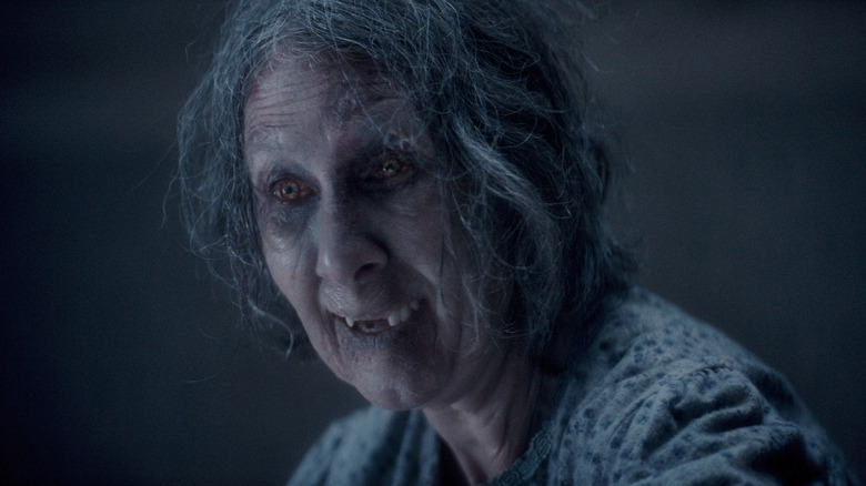 O femeie mai în vârstă care este posedată de Deadites care chicotesc în Evil Dead Burn