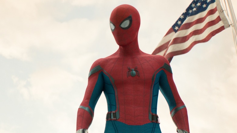 Tom Holland în rolul lui Peter Parker purtând costumul său de supererou și stând lângă un steag american în Spider-Man: Homecoming