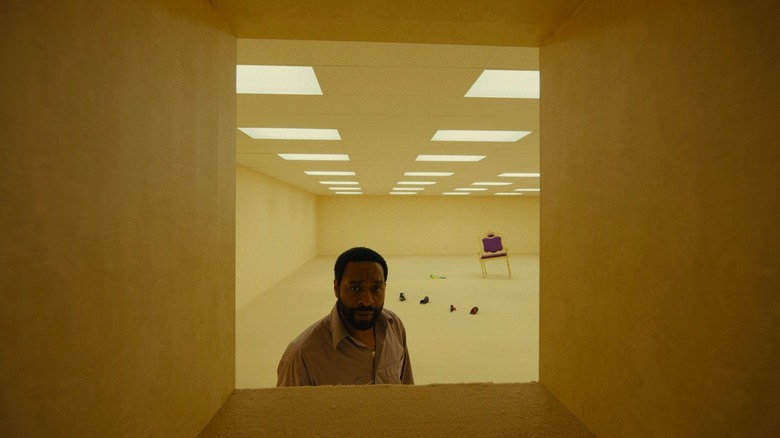 Chiwetel Ejiofor în rolul lui Clark stând într-o cameră goală de birou, plină cu resturi aleatorii și privind printr-un pasaj din peretele din Backrooms