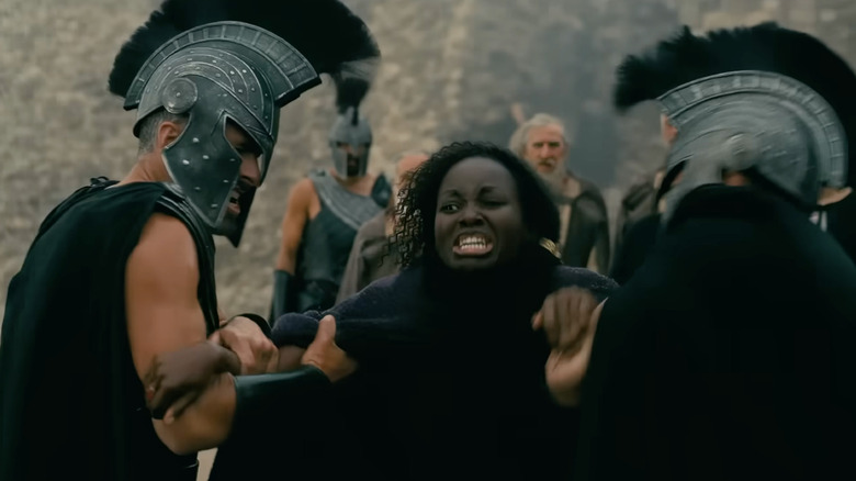 Lupita Nyong'o în rolul lui Clitemnestra care țipă de suferință în timp ce era reținută de doi soldați în Odiseea