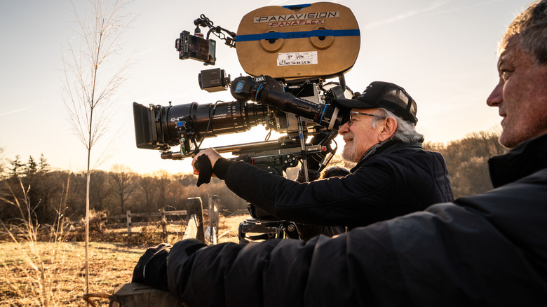 Regizorul Steven Spielberg ține o cameră Panavision și se uită prin lentilă într-un câmp deschis în platoul Zilei dezvăluirii