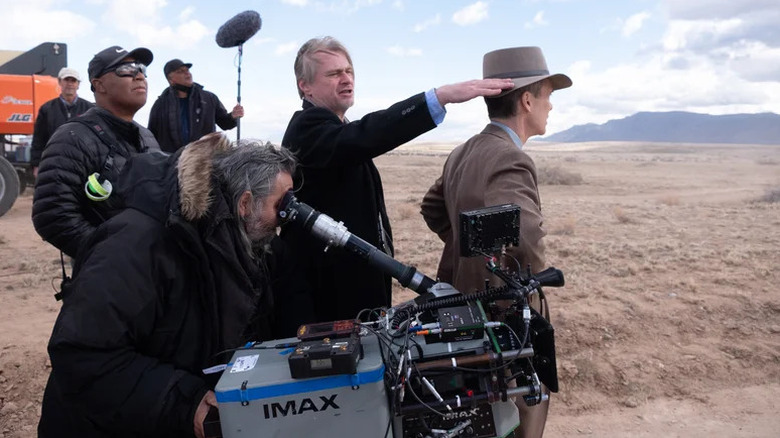 Christopher Nolan arată în depărtare în timp ce stă cu un echipaj de filmare în culisele lui Oppenheimer
