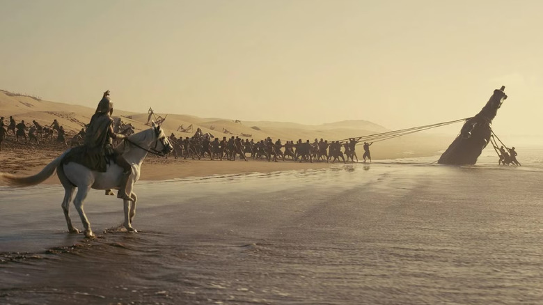 Bărbați care trag calul troian de pe o plajă în The Odyssey (2026)