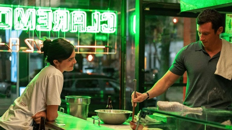 Monica Barbaro în rolul lui Allie, stând la tejghea, vorbind cu Callum Turner în rolul lui Owen, în timp ce el face o pizza în One Night Only