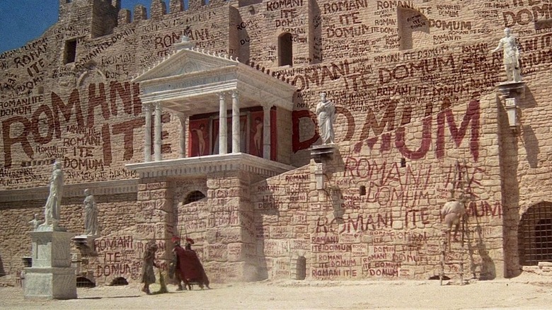 O clădire romană acoperită cu graffiti care spune „Romani Ito Domum” în Life of Brian