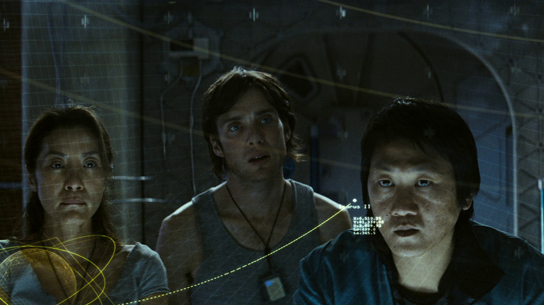 Michelle Yeoh în rolul lui Corazon, Cillian Murphy în rolul lui Robert și Benedict Wong în rolul lui Trey privind o diagramă în Sunshine